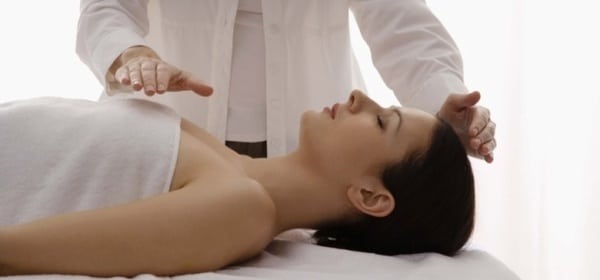 Pranoterapeuta che esegue un trattamento energetico senza contatto su una donna sdraiata