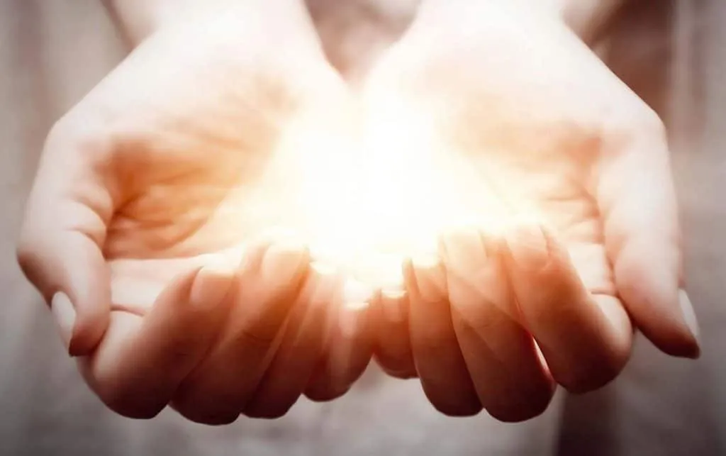 Mani aperte che emanano una luce calda, simbolo della pranoterapia e del significato del prano, rappresentazione di come funziona il curare con le mani secondo un pranoterapeuta.