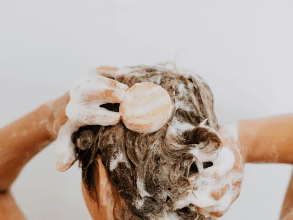Persona che lava i capelli con shampoo solido naturale producendo una leggera schiuma