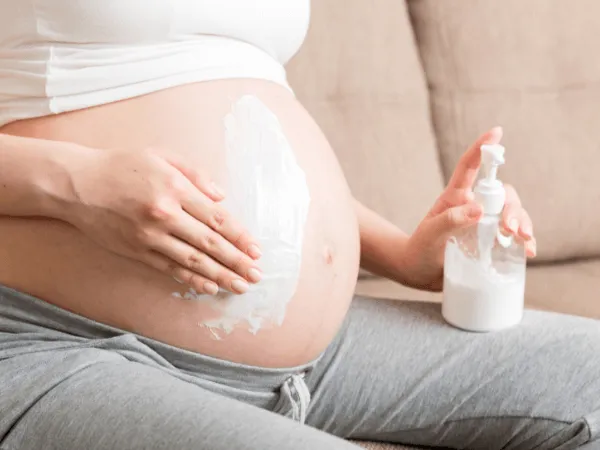 Donna incinta applica crema preventiva contro le smagliature sull’addome